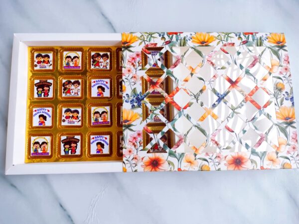 Real&Natural Raksha Bandhan chocolate gift box with 20 assorted chocolates in festive wrappers, displayed in a floral designer box with a transparent patterned lid."